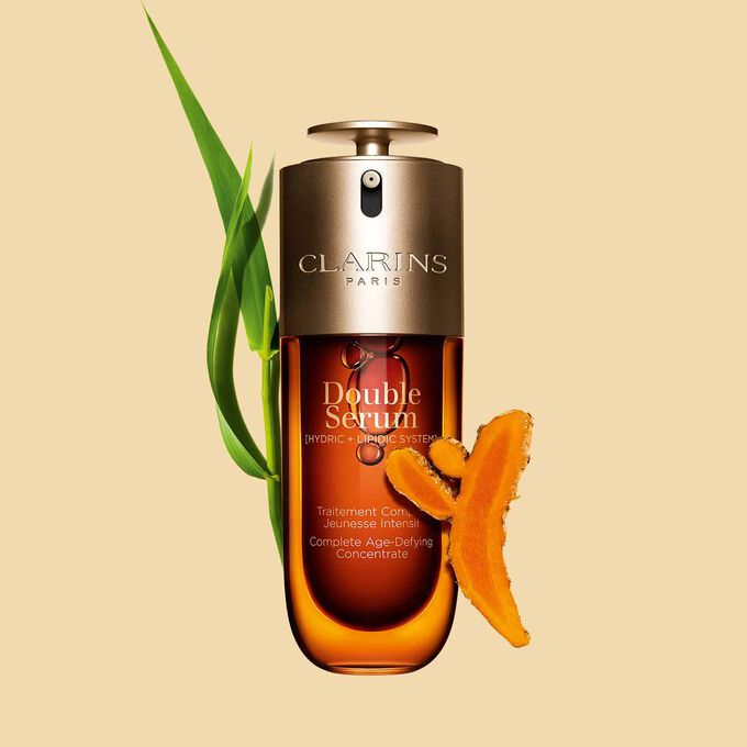 Packshot of the Clarins Double Serum displayed in front of its ingredient, including curcuma, on a gold background